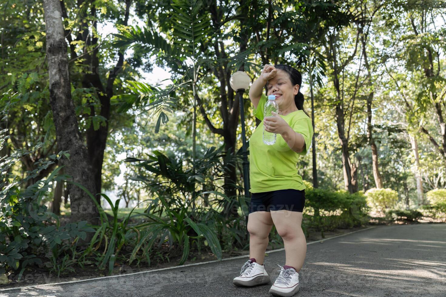 Petite Woman Jogging in a Lush Green Park on a Sunny Day, Staying Active and Healthy in Nature, Wearing Casual Sportswear and Holding a Water Bottle photo