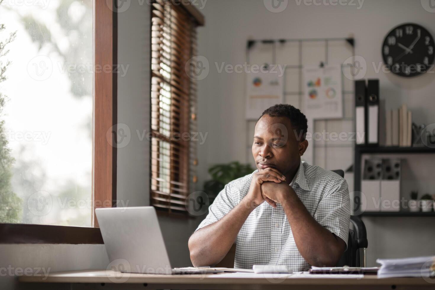 African American businessman feeling stressed while working using laptop Take notes on documents in the office and prepare work reports. photo