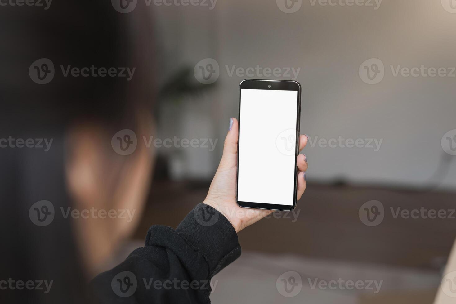 Young Woman Holding Smartphone with Blank White Screen in Modern Indoor Setting, Perfect for Mockups and Digital Content photo