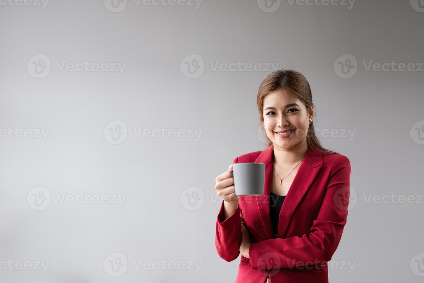 confidente negocio mujer en rojo chaqueta de sport participación café taza, sonriente, y en pie en contra minimalista antecedentes - profesional y empoderado hembra líder en moderno corporativo ambiente foto