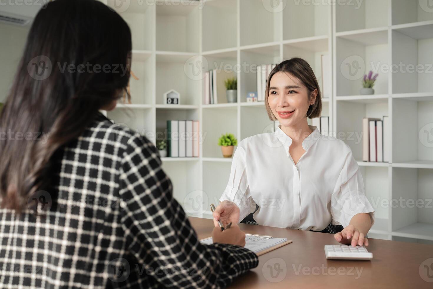 Two Asian businesswomen discussing financial documents with calculator at office desk. Concept of business finance and professional consultation photo