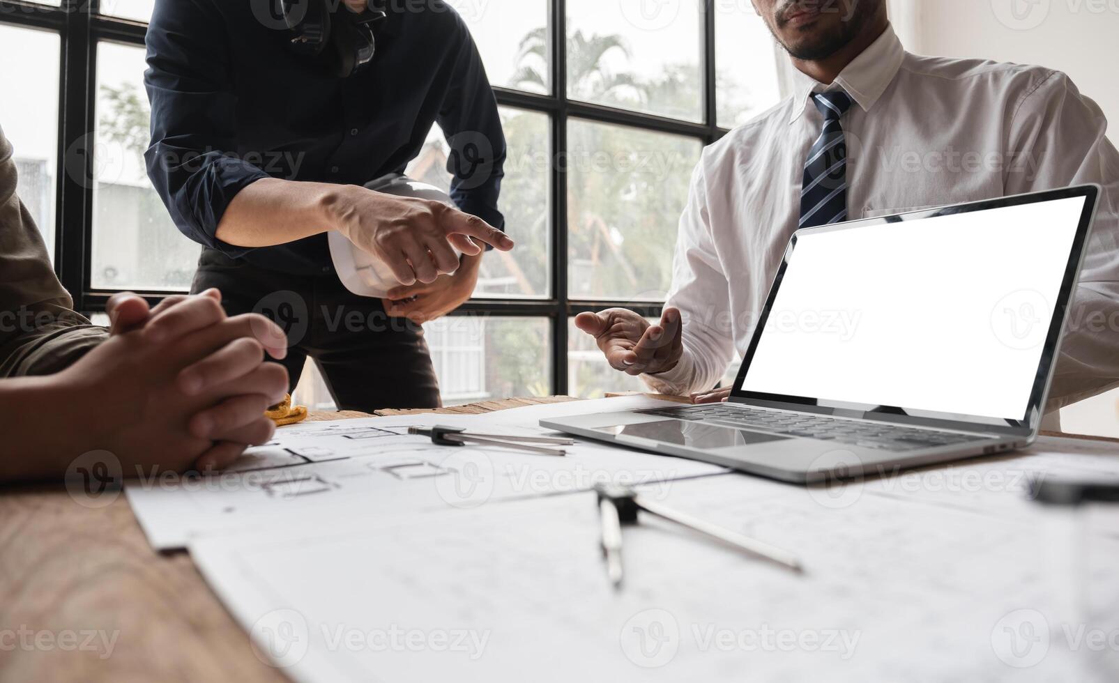 Engineering Team Collaborating on Work Plans Around a Table with Laptop and Blueprints photo
