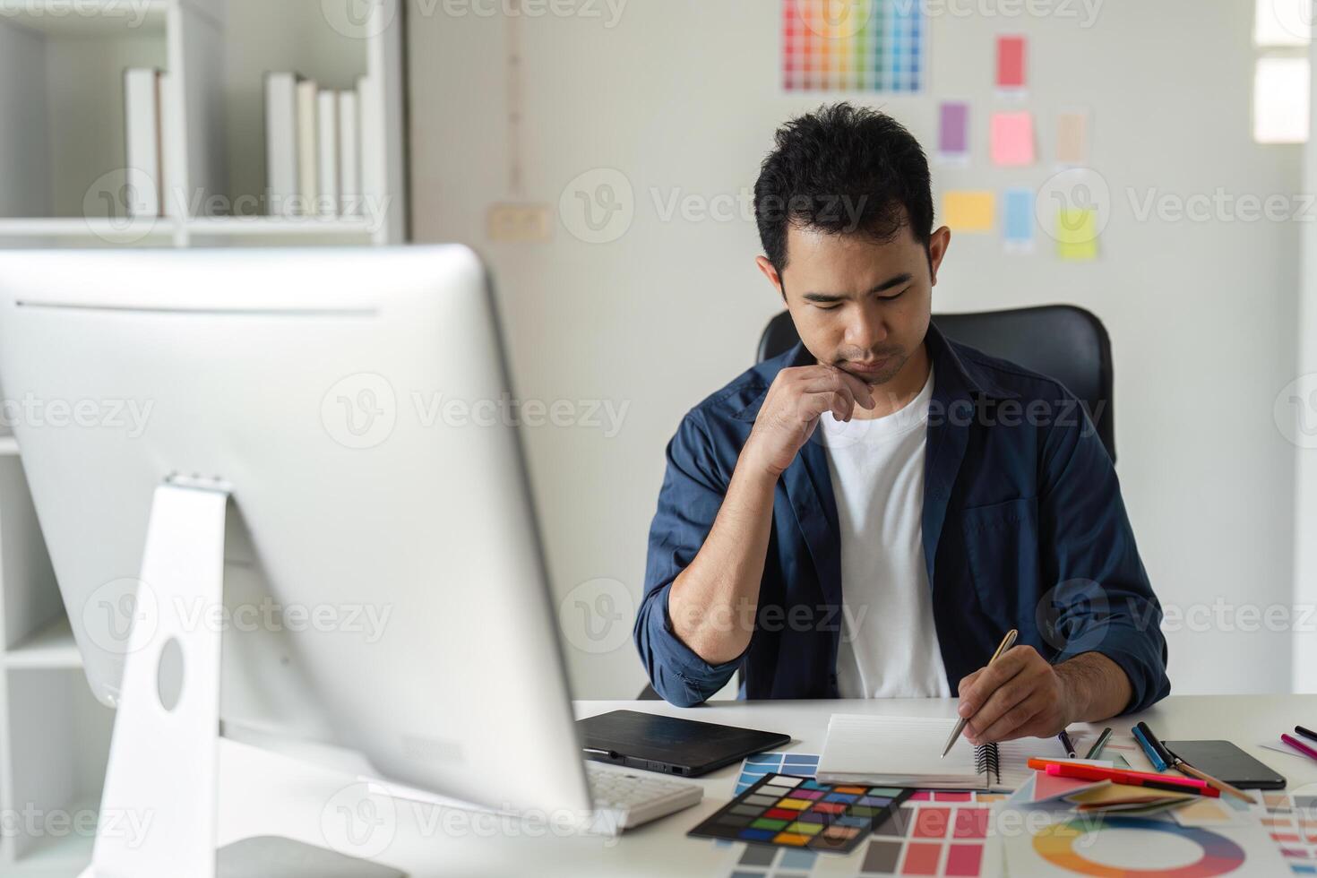 Young Male Graphic Designer Focused on Creative Project at Modern Workspace with Computer and Color Swatches photo