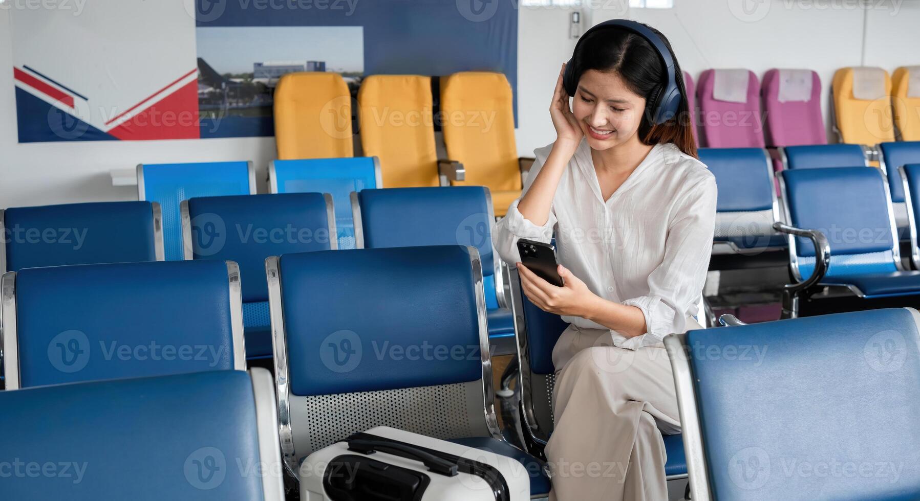 Asian woman listening to music on smartphone in airport waiting area. Concept of travel, technology, and relaxation photo