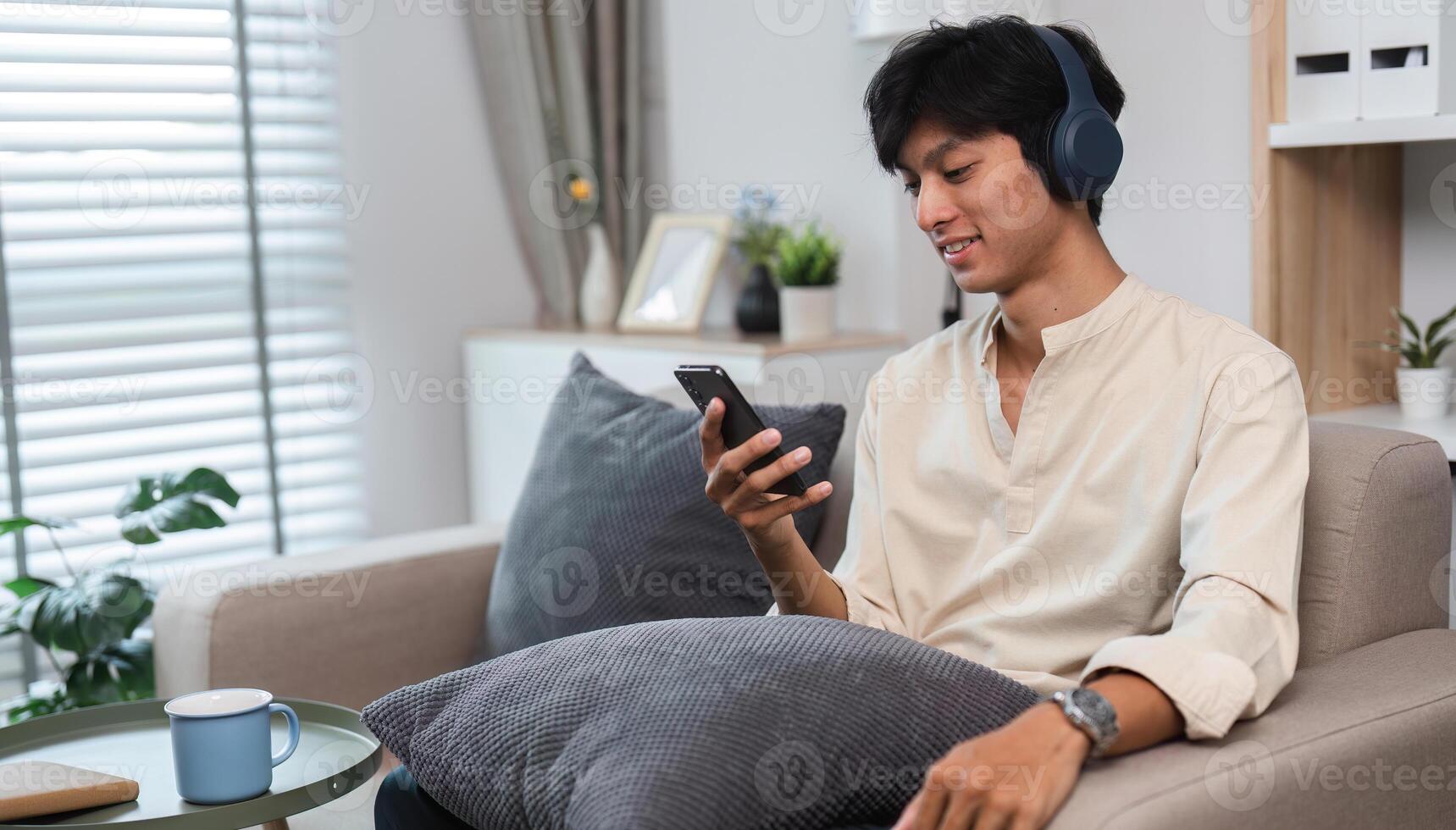 Young Man Relaxing on Sofa in Modern Living Room While Exploring Social Media on Smartphone photo