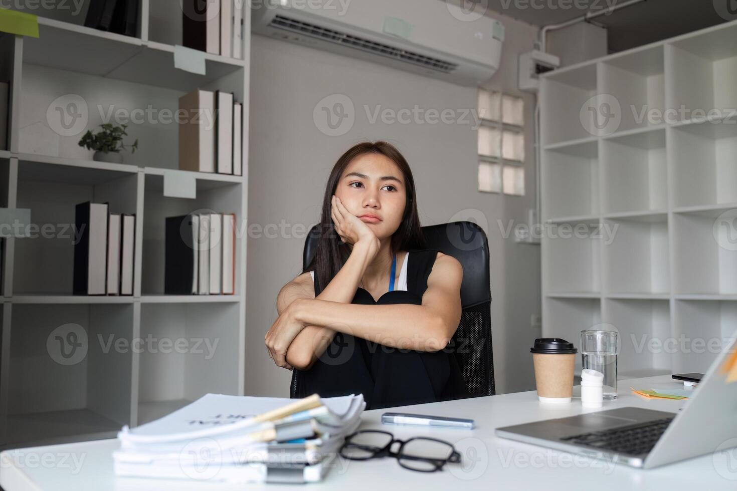 Bored Woman at Work Sitting at Desk in Modern Office with Laptop and Documents, Feeling Uninspired and Unmotivated During Work Hours photo