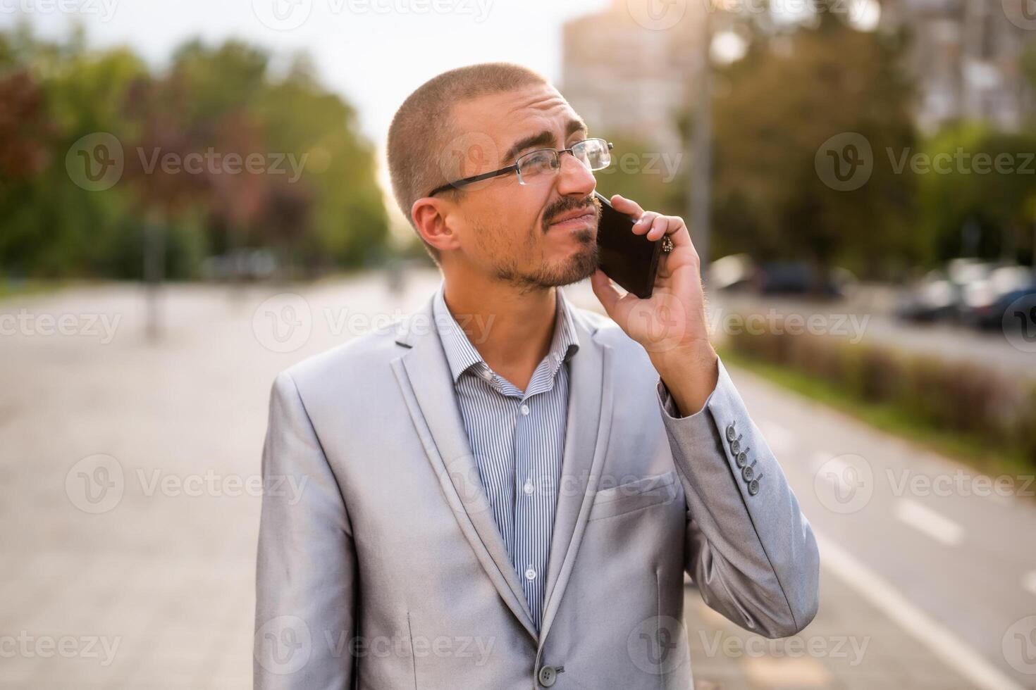 Portrait of distraught businessman who is talking on phone. Young businessman standing in the street and using smartphone. photo