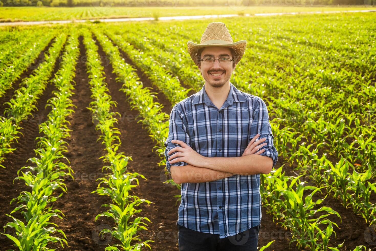 Happy farmer standing in his corn field. Successful farmer smiling in agricultural field on sunny day. photo