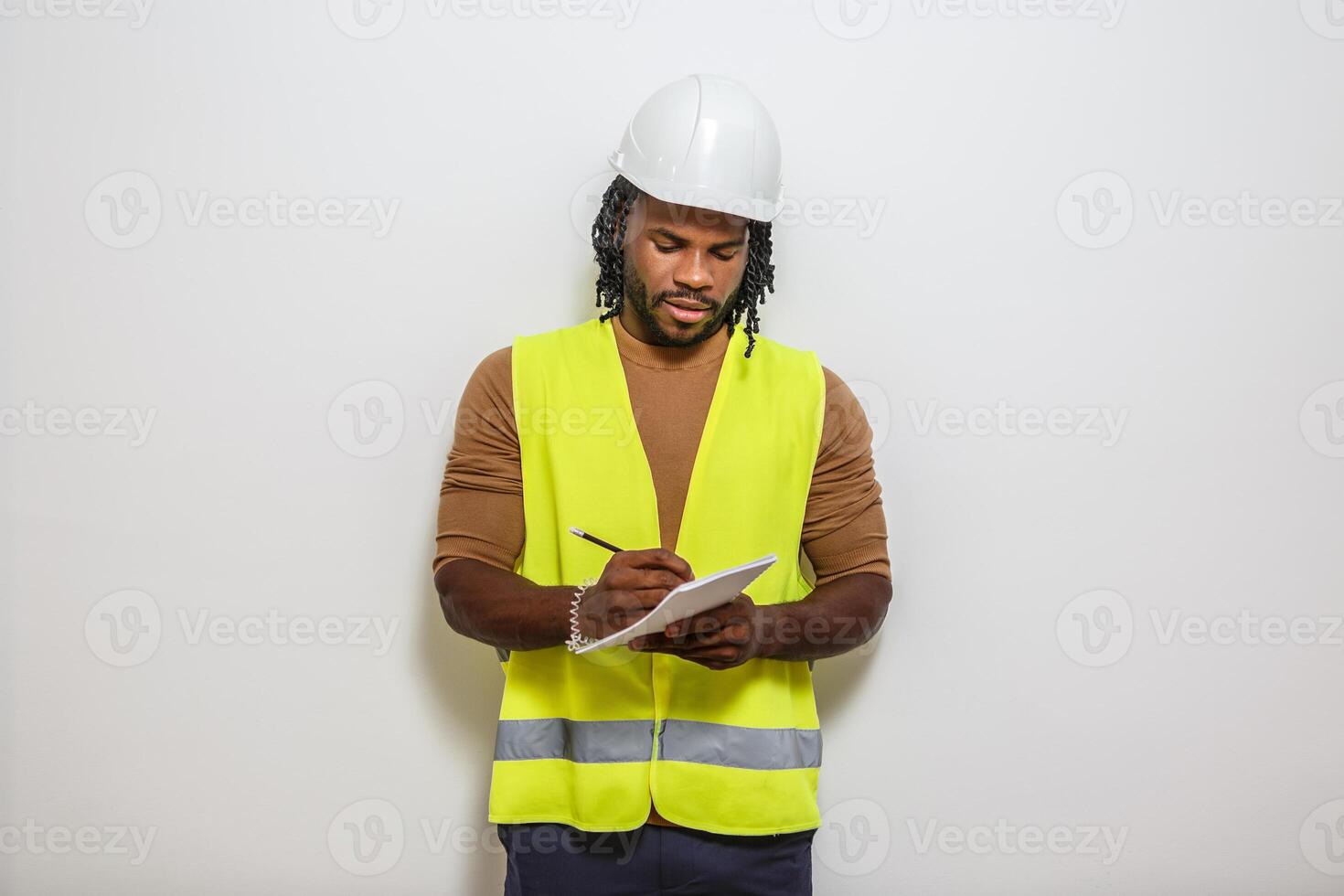 A construction worker in safety gear takes notes in front of a white background. photo