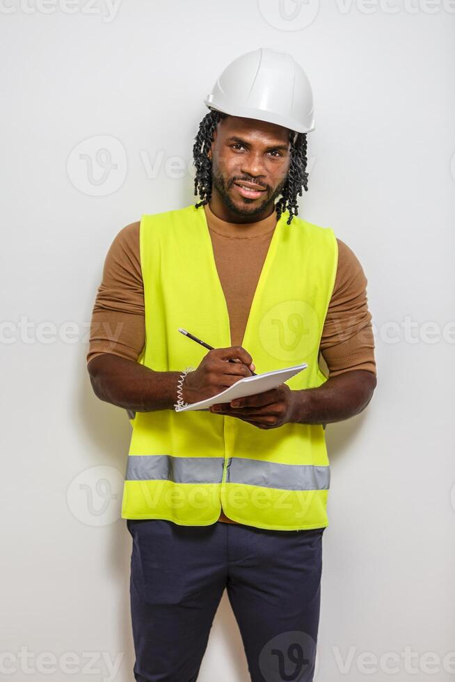 A construction worker in safety gear takes notes in front of a white wall. photo