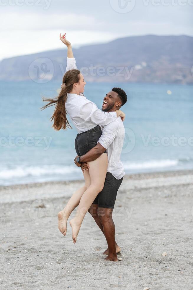 Couple joyfully celebrating on a sandy beach with ocean waves in the background during a cloudy day photo