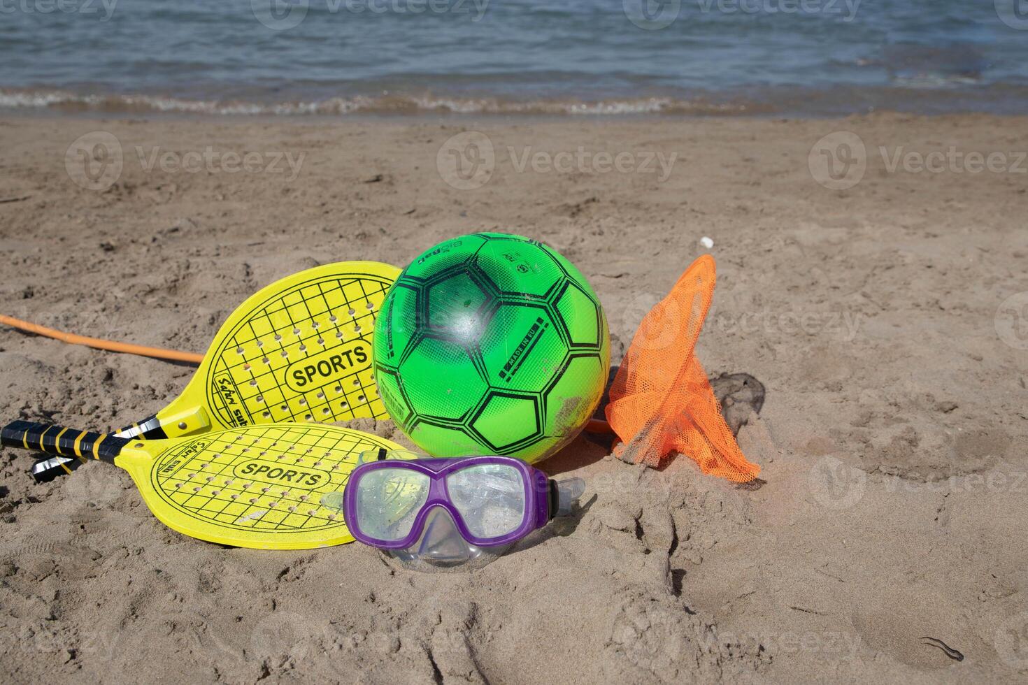 Beach tennis racket and ball of yellow color,swimming mask ,and beach playing ball on tne beach.Copy space.Summer sport background. photo