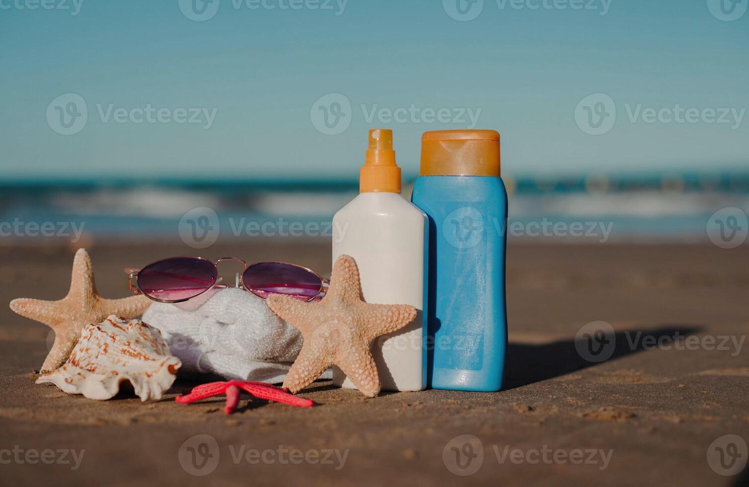 Beach essentials on sandy shore with sunscreen, starfish, and sunglasses. photo