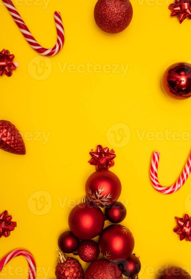Top view photo tree lined with Christmas tree decorations, christmas tree toys of red colour, christmas lollipops on yellow background for greeting card. Xmas backdrop with space for text.Copyspace.Vertical photo.