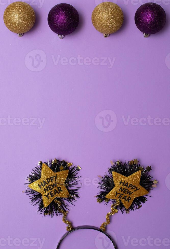New Year's decor in the form of a golden star shape with black colour text Happy New Year , christmas tree toys on purple background.Copy space.Top view photo.Flatlay.Vertical photo. photo
