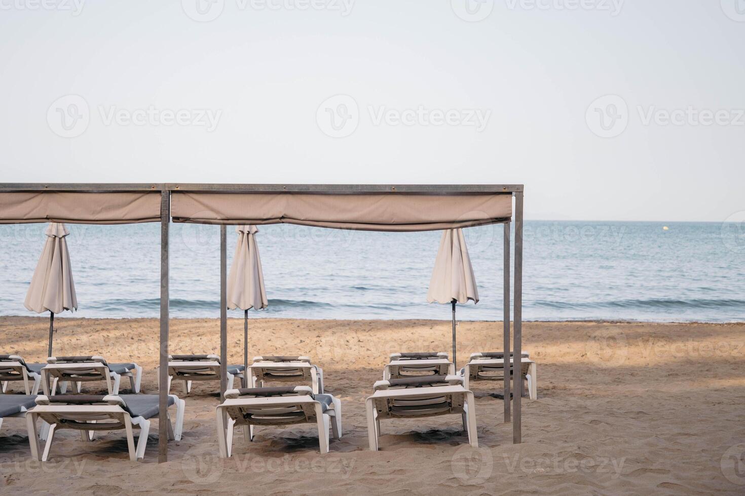 Scenic view in sunny morning to a chaise lounges and umbrellas on the sandy beach without people,sea on the background.Copy space. High quality photo