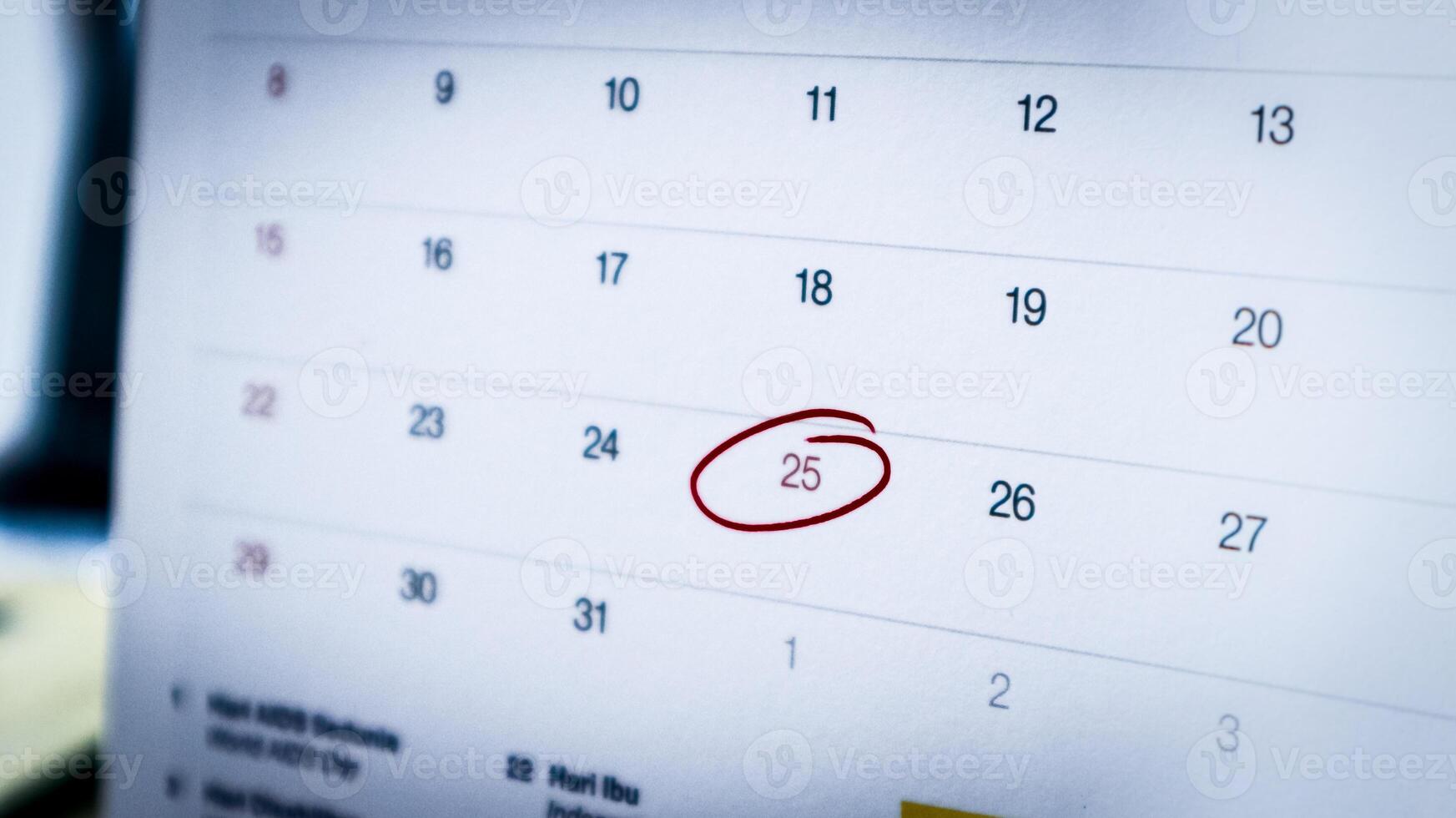 close-up of December 25, 2024, on an office calendar, circled in red marker to indicate a holiday, with a blurred office workspace in the background. photo