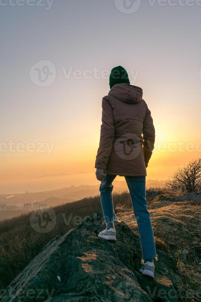 Girl in a jacket and a hat on the mountain during sunset photo