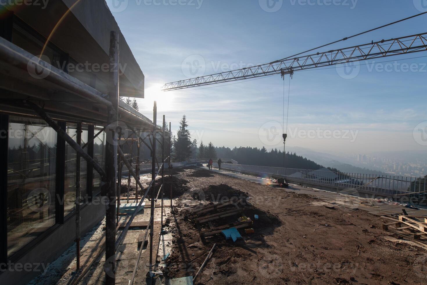 The exterior of a business building under construction is surrounded by trucks, cranes, and various construction materials, creating a bustling scene of an expansive industrial worksite in progress photo