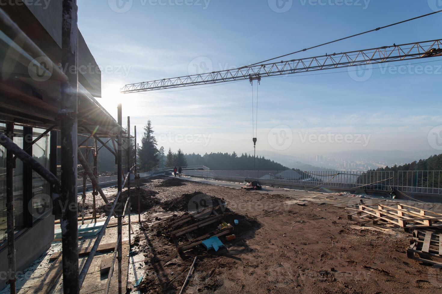 The exterior of a business building under construction is surrounded by trucks, cranes, and various construction materials, creating a bustling scene of an expansive industrial worksite in progress photo