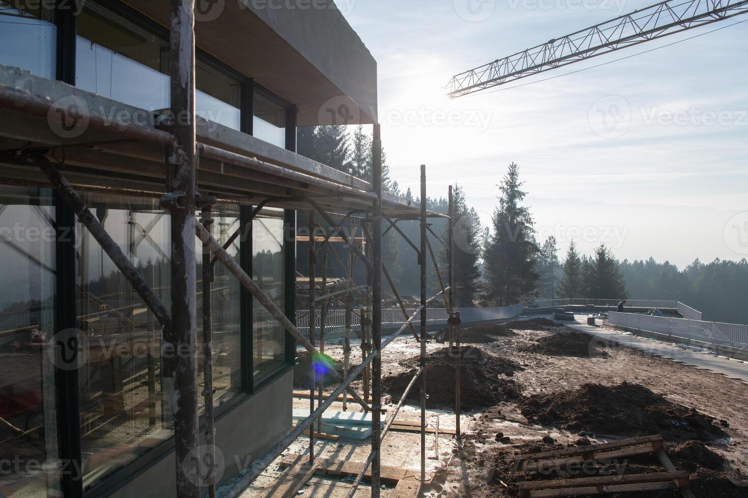 The exterior of a business building under construction is surrounded by trucks, cranes, and various construction materials, creating a bustling scene of an expansive industrial worksite in progress photo