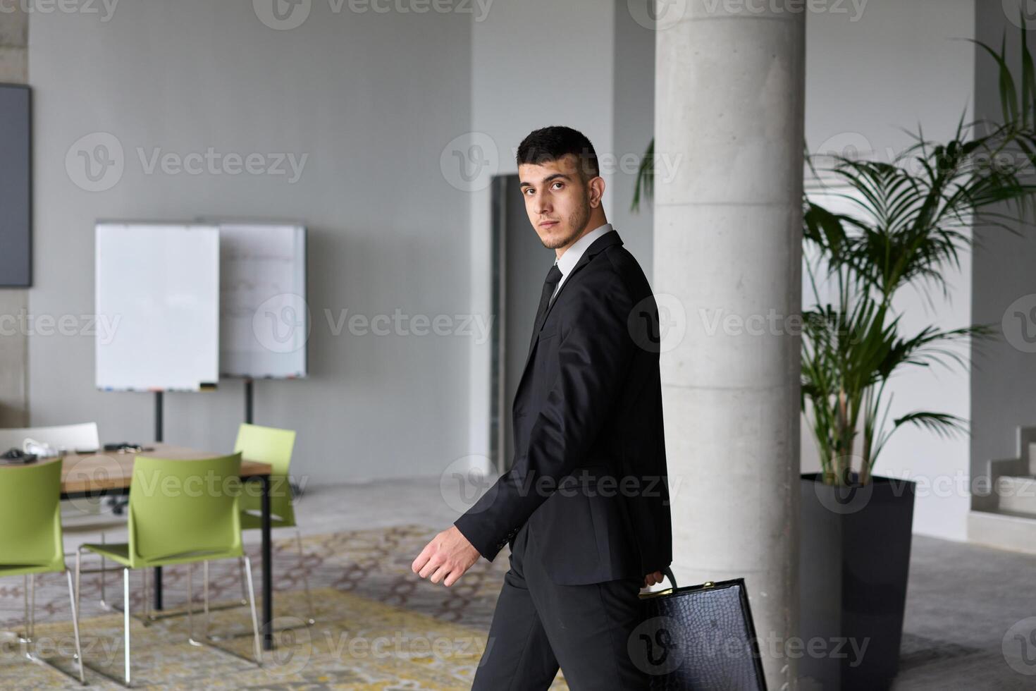 A determined businessman in a black suit confidently walks through the office, embodying professionalism and focus as he heads towards new challenges photo