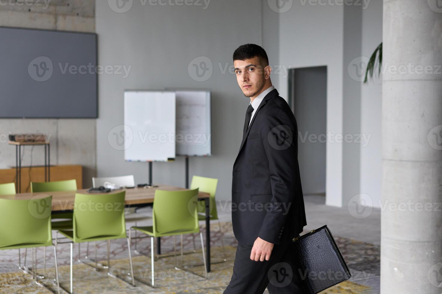 A determined businessman in a black suit confidently walks through the office, embodying professionalism and focus as he heads towards new challenges photo