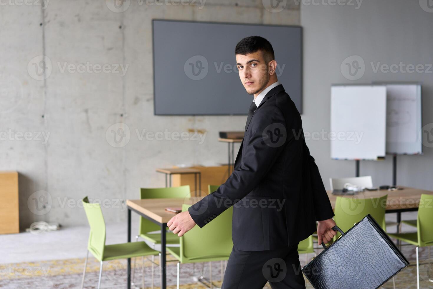 A determined businessman in a black suit confidently walks through the office, embodying professionalism and focus as he heads towards new challenges photo