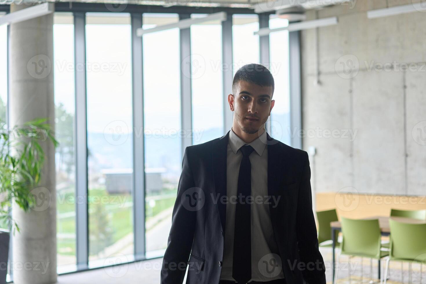 A determined businessman in a black suit confidently walks through the office, embodying professionalism and focus as he heads towards new challenges photo