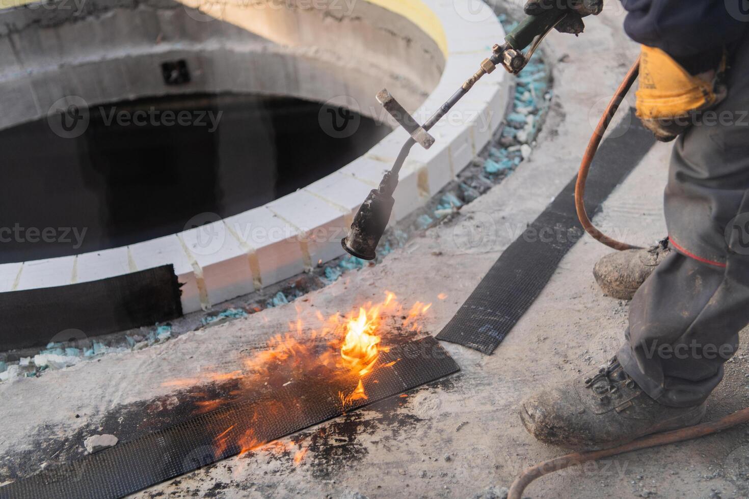 An industrial worker uses fire to soften a rubber underlay for floor insulation, showcasing precision and skill in a critical step of the construction process photo