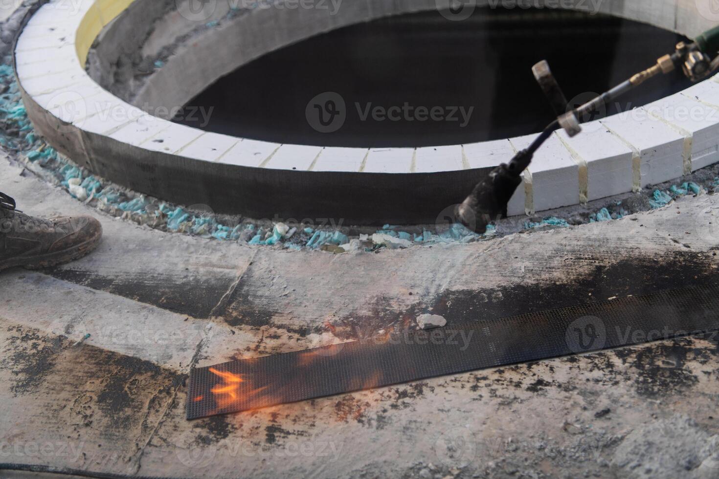 An industrial worker uses fire to soften a rubber underlay for floor insulation, showcasing precision and skill in a critical step of the construction process photo