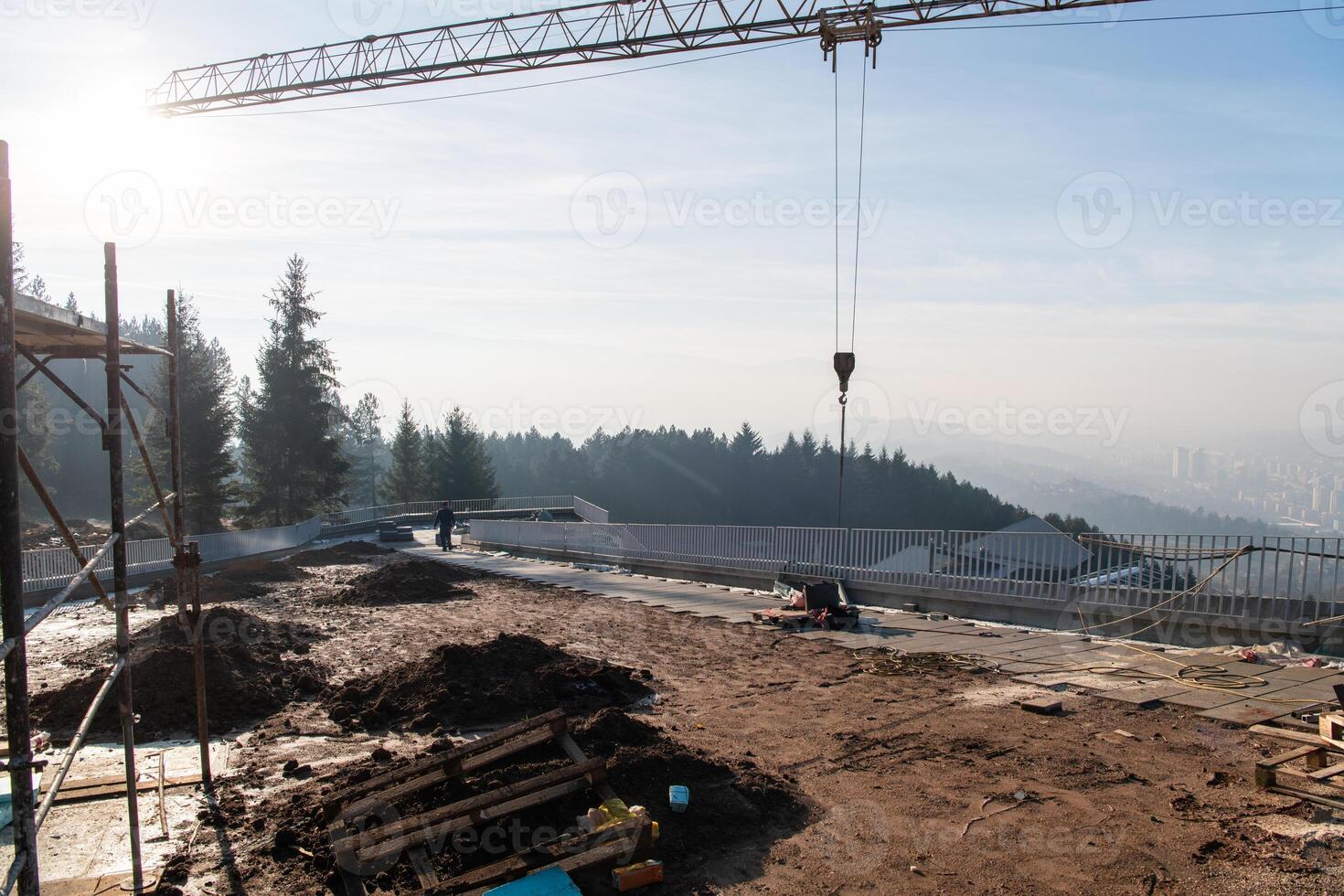 The exterior of a business building under construction is surrounded by trucks, cranes, and various construction materials, creating a bustling scene of an expansive industrial worksite in progress photo