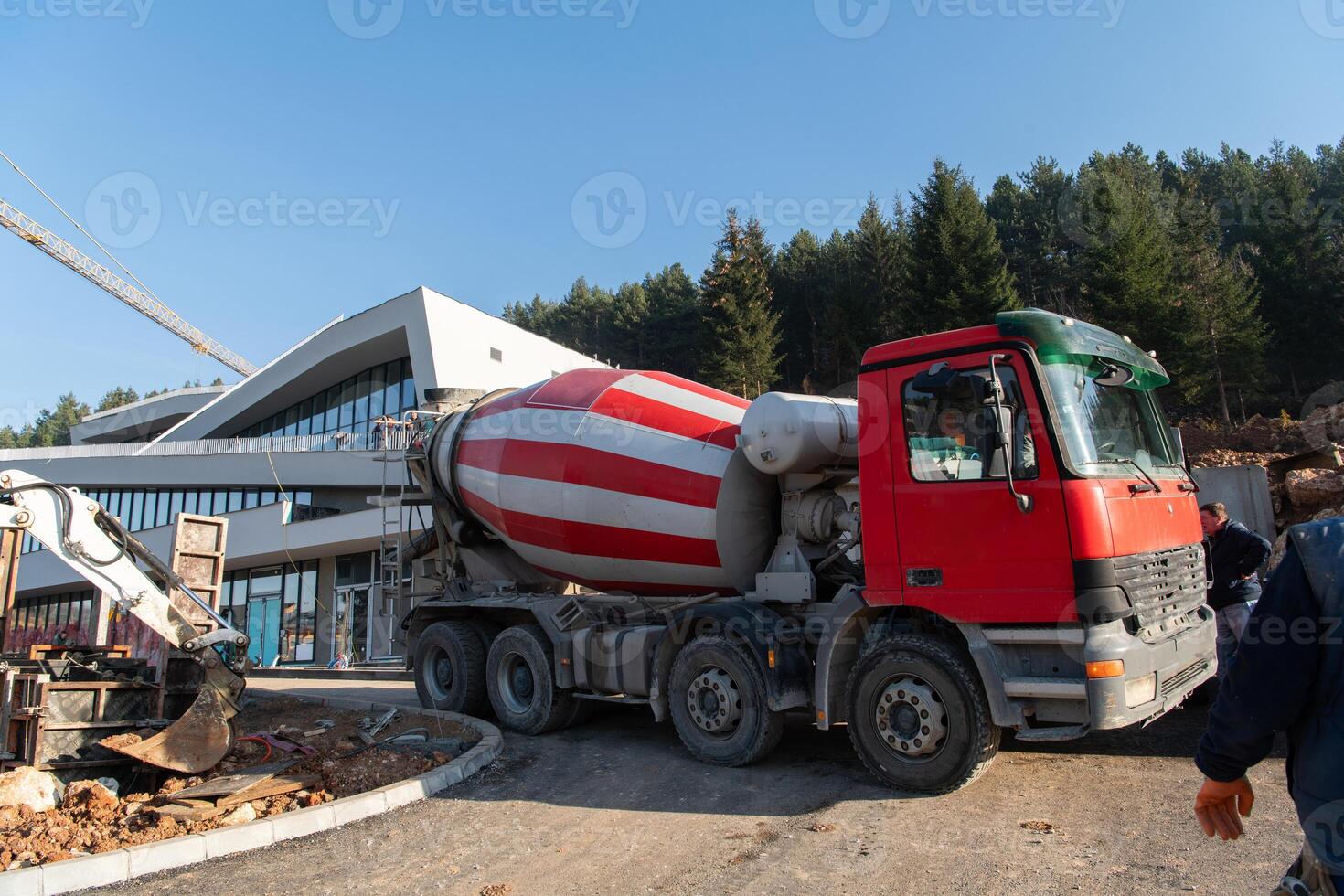 The exterior of a business building under construction is surrounded by trucks, cranes, and various construction materials, creating a bustling scene of an expansive industrial worksite in progress photo