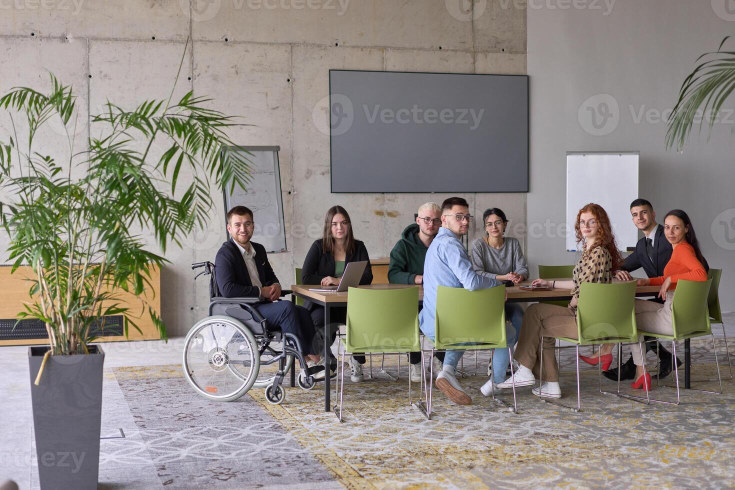 A diverse group of business professionals sitting in an office meeting with their director, who is in a wheelchair, fostering collaboration, leadership, and inclusivity photo