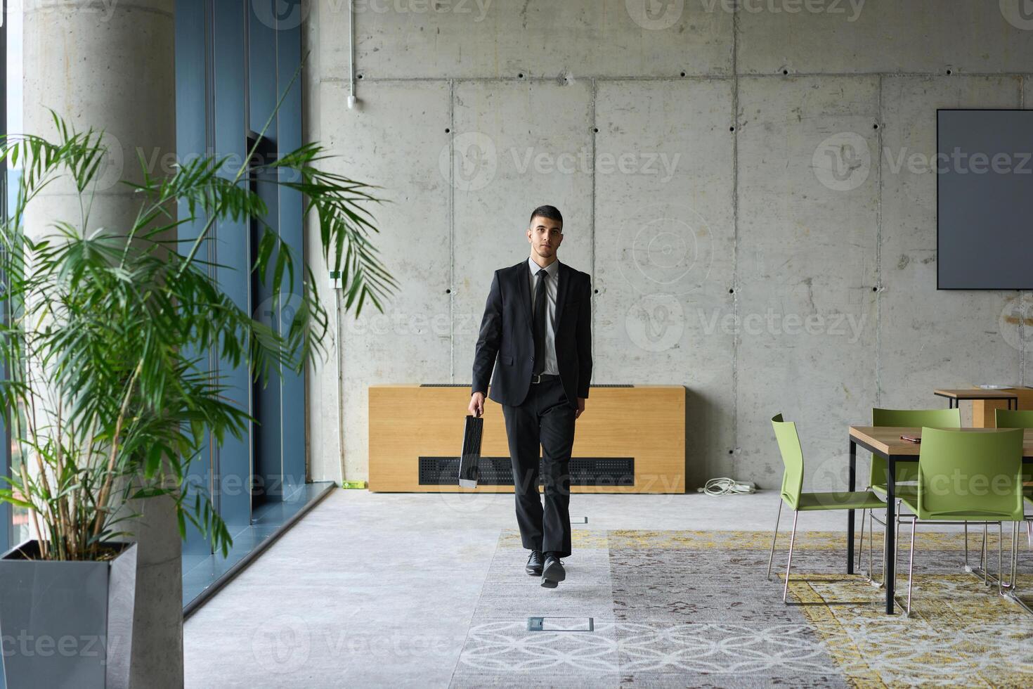 A determined businessman in a black suit confidently walks through the office, embodying professionalism and focus as he heads towards new challenges photo