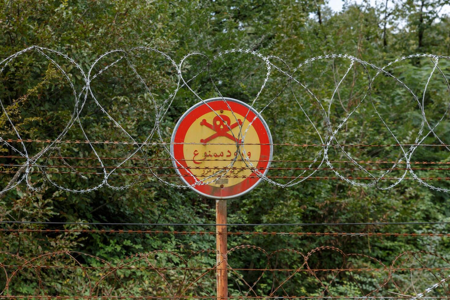Gilan Province, Iran - September 28, 2024 - A warning sign near the fortified Iran-Azerbaijan border, with barbed wire and thick vegetation, indicates restricted access. photo