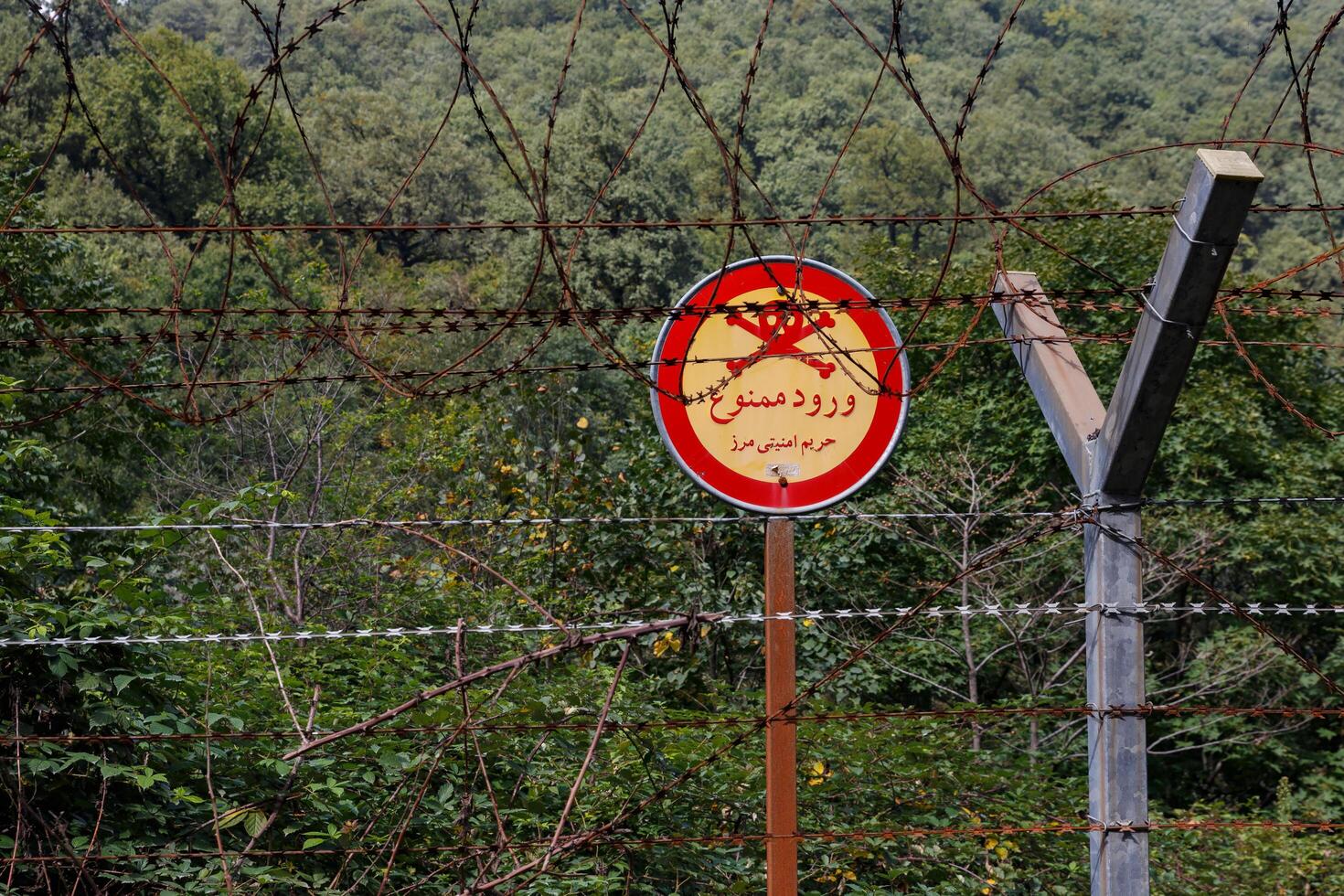 Gilan Province, Iran - September 28, 2024 - Barbed wire and warning signs delineate the border territories of Iran and Azerbaijan, surrounded by greenery and vegetation. photo