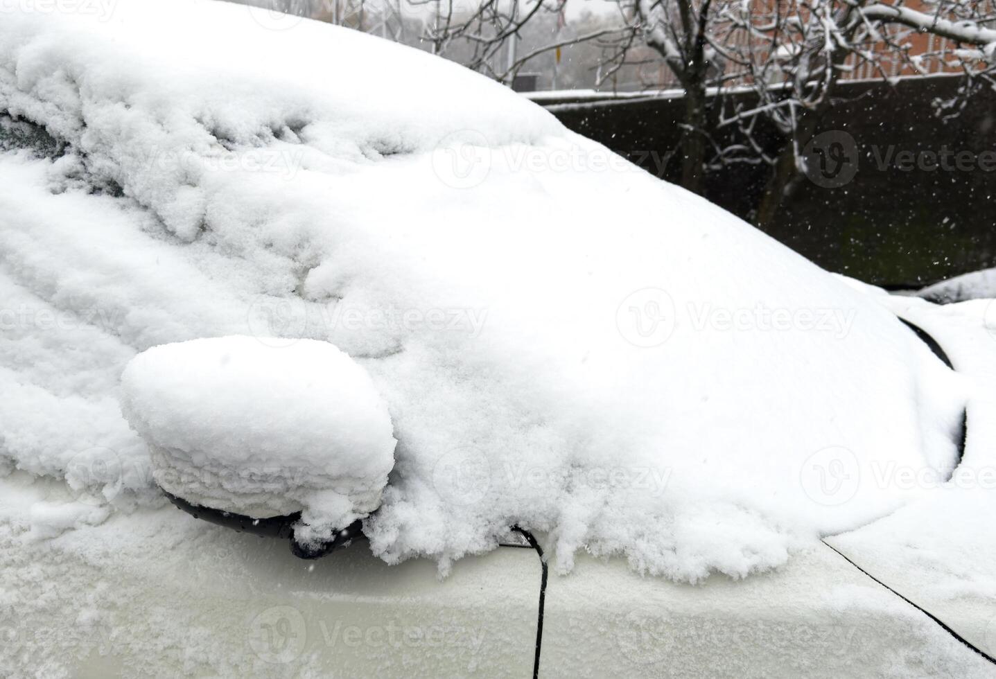 The car drives through the snow, the bright winter sun shines against the background of the forest. Close-up rearview mirror. The vehicle is covered with snow. Snowing. photo