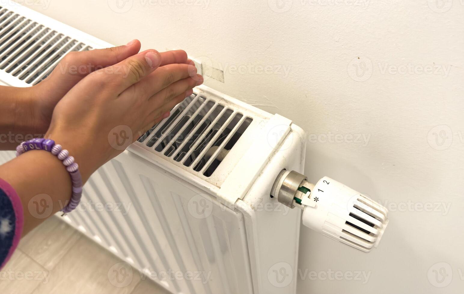 Closeup of woman warming her hands on the heater at home during cold winter days, top view. Female getting warm up her arms over radiator. Concept of heating season, cold weather. photo