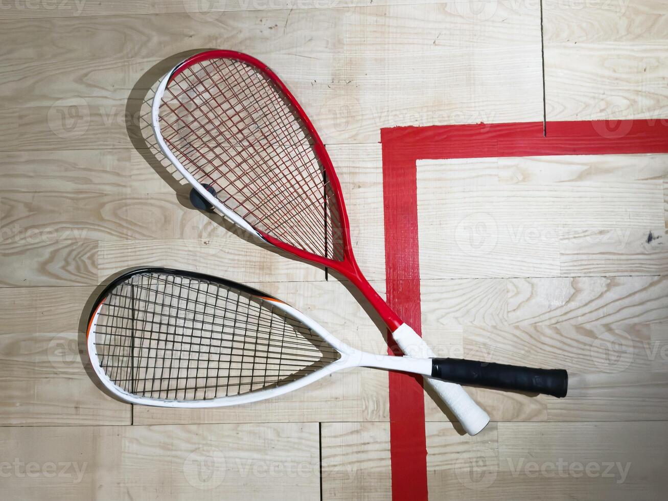 Two rackets and two squash balls lie on the parquet floor. Horizontal photo