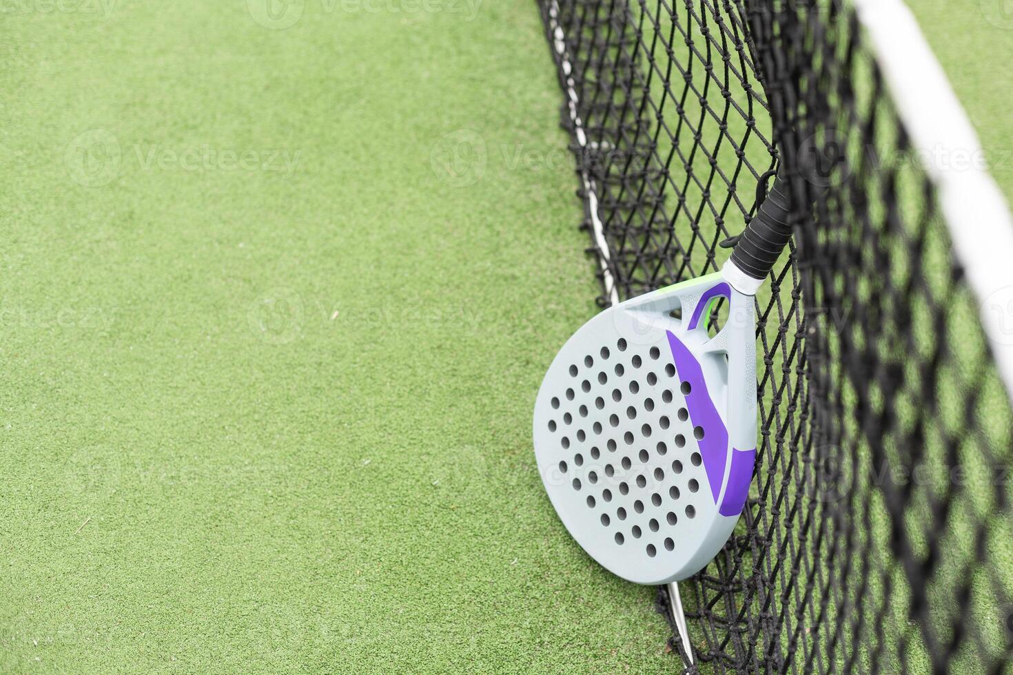 Closeup view of a paddle racket and balls in a padel tennis court near the net. Green background with white lines. Sport, health, youth and leisure concept. Sporty equipment. photo