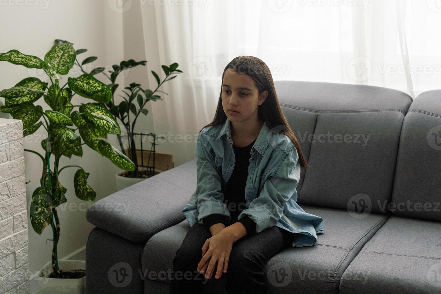 girl wearing blue shirt sitting on couch at home and looking away. Lifestyle child portrait. photo