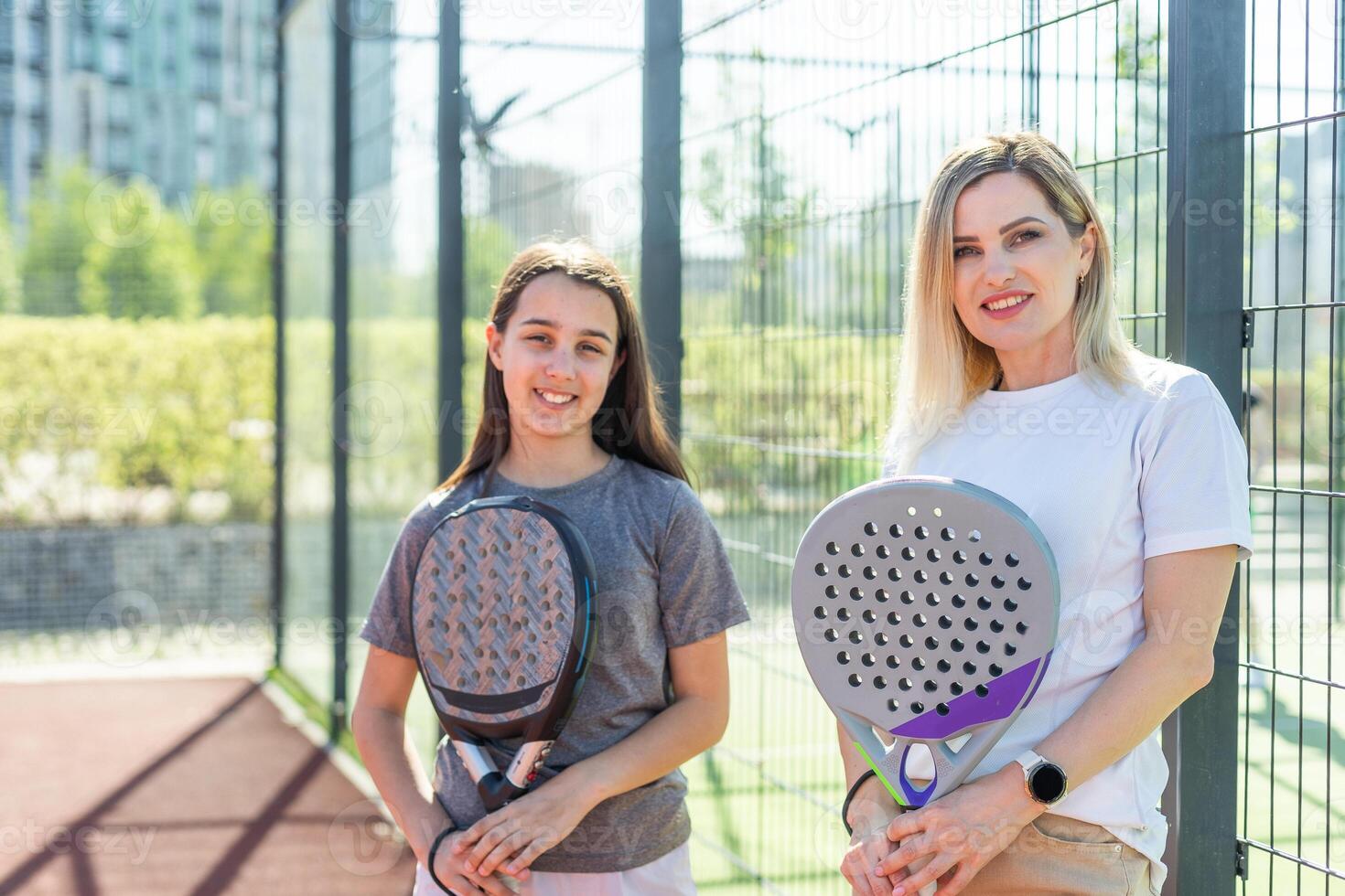 Cheerful coach teaching child to play padel tennis while both standing on tennis court photo