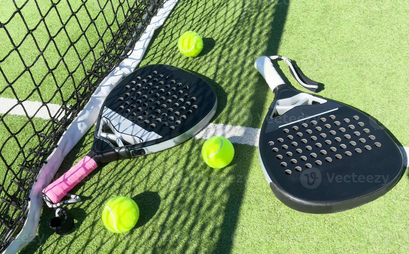 Yellow balls on grass turf near padel tennis racket behind net in green court outdoors with natural lighting. Paddle is a racquet game. Professional sport concept with copy space. photo