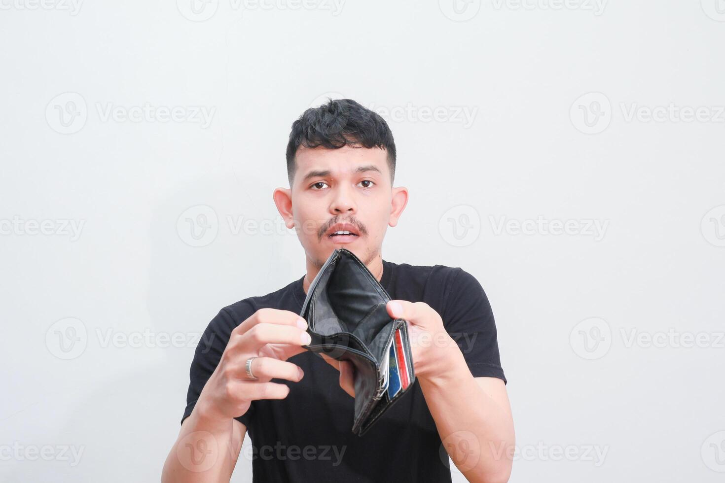 a portrait of asian young man holding his empty wallet with sad expression photo