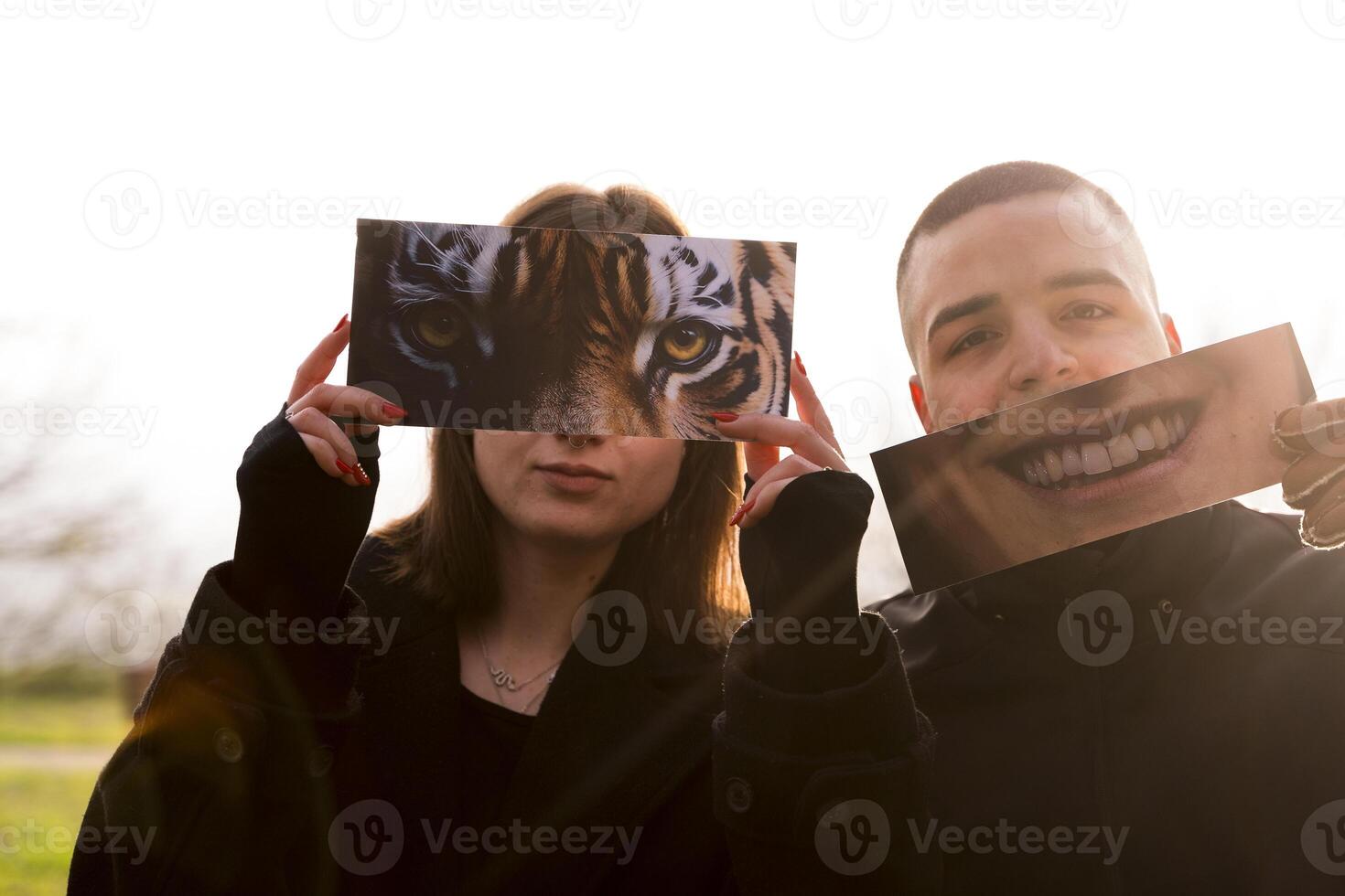 portrait of two young lovers having fun showing a fantasy pictures partially covering their faces in a public park in winter photo