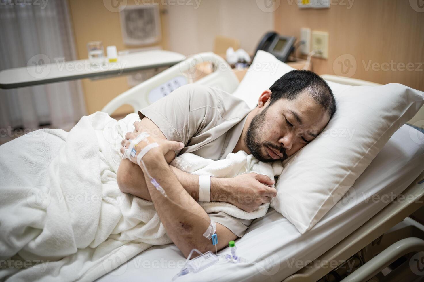 A male patient lies in a hospital room receiving treatment, exhausted and lonely. photo
