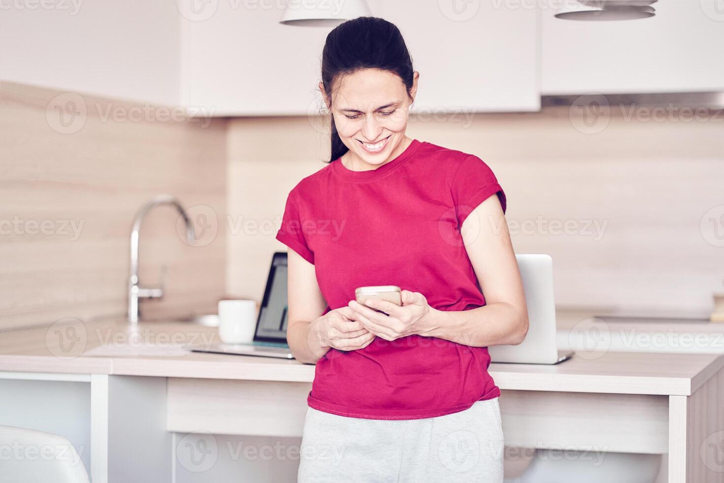 A happy woman checks social networks while holding a smartphone at home. Smiling young woman using a mobile phone app, playing games, shopping online, ordering delivery photo