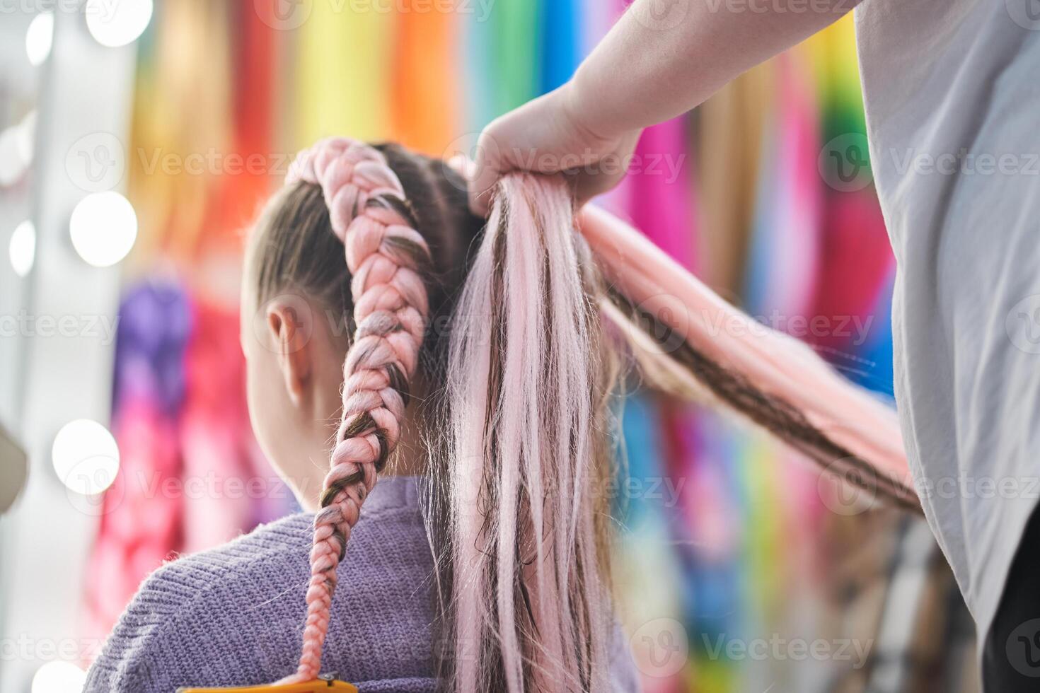 A rear view of the hands of the master who weave the kanekalon material into the hair. The master braids the child's pigtails from a pink kanekalon. With space to copy photo