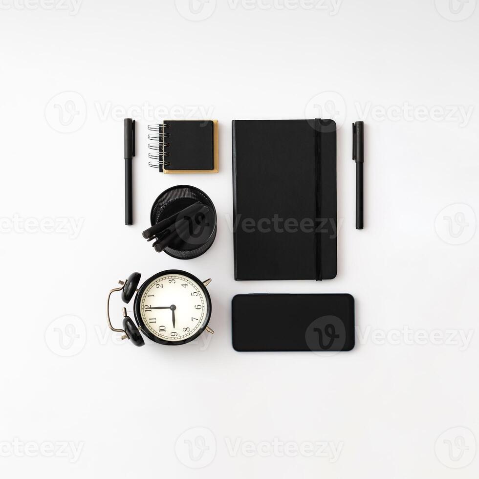 Trendy arrangement made with black notebooks, pens, alarm clock and phone on white background. Minimal business concept. Creative office objects idea. Black and white flat lay. photo